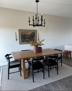 a dining room table with black chairs and a painting on the wall in the background