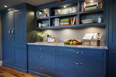 a kitchen with blue cabinets and marble counter tops, along with bookshelves on the wall