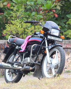 a motorcycle parked on the side of a road next to some bushes and trees in front of a stone wall