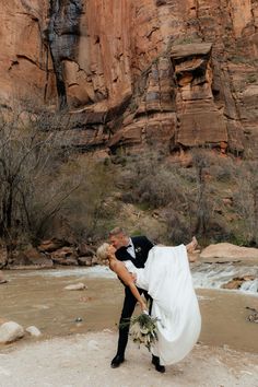 a bride and groom are kissing in front of a mountain side waterfall at their wedding