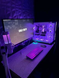 a computer desk with a keyboard, mouse and monitor lit up by purple lighting in the dark