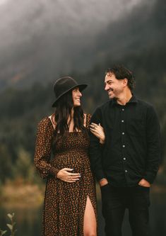 a man and woman standing next to each other in front of a body of water