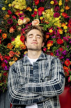 a man standing with his arms crossed in front of a bunch of flowers on the wall