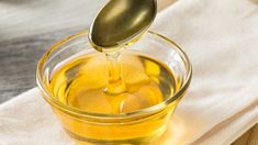 a glass bowl filled with oil on top of a white towel next to a spoon