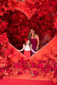 mother and daughter in heart shaped photo booth with red flowers on the wall for valentine's day