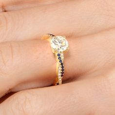 a woman's hand with a diamond and sapphire engagement ring on it, set in yellow gold