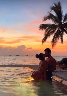 a man and woman sitting in the water at sunset with their backs to each other