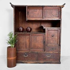 an old wooden cabinet with two vases next to it and a potted plant