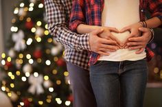 two people standing in front of a christmas tree with their hands on their stomach - stock photo - images