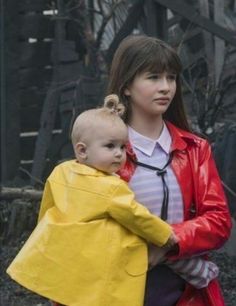 a woman carrying a child in a yellow raincoat and red jacket on her back