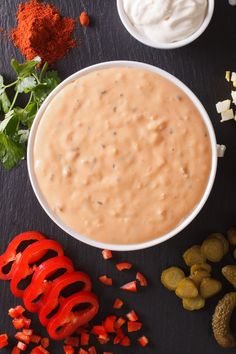 a white bowl filled with dip surrounded by sliced peppers, cheese and other ingredients on a black surface