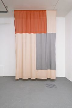 an orange and grey curtain hanging in front of a white wall with a grate on the floor