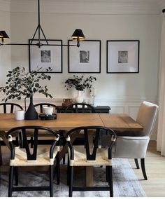 a dining room table with chairs and pictures on the wall above it, along with potted plants