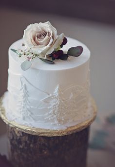 a three tiered cake with white frosting and a flower on top is sitting on a table