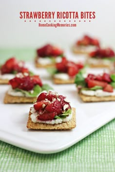 small crackers with strawberries and cream cheese on them sitting on a white surface