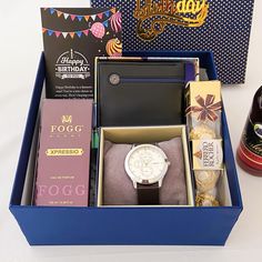 a birthday gift box with books, watch and other items in it on a table