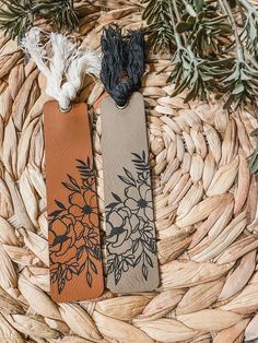 two leather bookmarks sitting on top of a wicker basket next to some plants