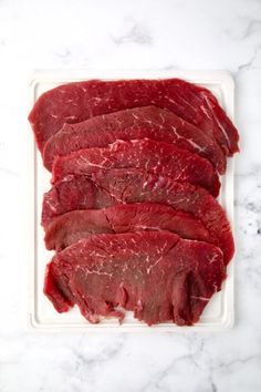 sliced beef on a cutting board sitting on a marble counter top, ready to be cooked