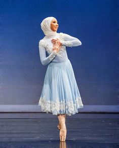 a woman in a blue dress and head scarf is standing with her hands on her hips