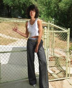 a woman standing in front of a fence with her hand on her hip and looking at the camera