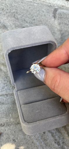 a woman's hand holding an engagement ring in a velvet box on the ground