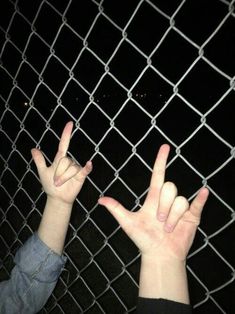 two hands reaching up through a chain link fence