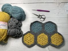 two crocheted mitts, yarn and scissors on a white wooden table with some knitting supplies