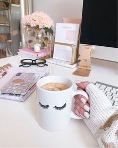 a woman is holding a coffee cup with eyelashes on it and her computer in the background