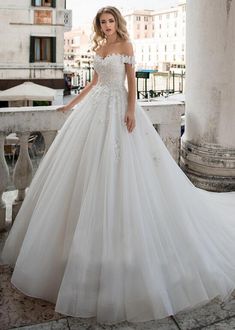 a woman in a white wedding dress standing on a balcony with her hand on her hip