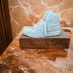 a pair of white sneakers sitting on top of a wooden block in front of a marble wall