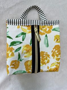 a yellow and white flowered purse with black zippers