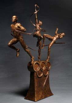 a bronze statue of two men on top of each other with the olympic rings in front of them