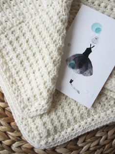 a white knitted blanket sitting on top of a woven basket next to a card