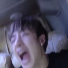 a young man with his mouth open in the back seat of a car while holding a cell phone to his ear