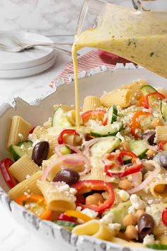 someone pouring dressing over a pasta salad in a bowl