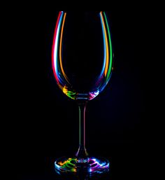 a colorful wine glass sitting on top of a black table next to a dark background