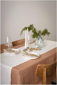 the table is set with white plates, silverware and greenery in a glass vase