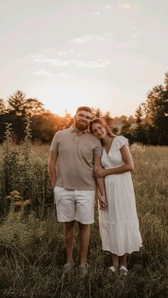 a man and woman standing in tall grass at sunset