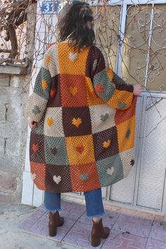 a woman standing on the sidewalk wearing a multicolored crocheted blanket