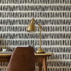 a brown chair sitting next to a wooden desk in front of a wall with black and white designs on it