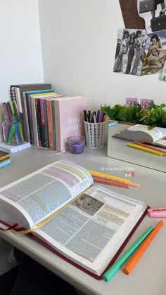 an open book sitting on top of a table next to books and pencils in front of it