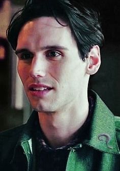 a close up of a person wearing a green jacket and looking at the camera with a serious look on his face