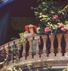 a woman wearing a red hat and sunglasses sitting on a balcony next to pink flowers