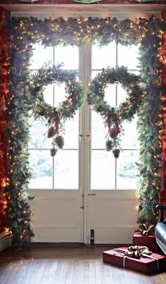 christmas wreaths and presents are on the floor in front of two windows with red curtains