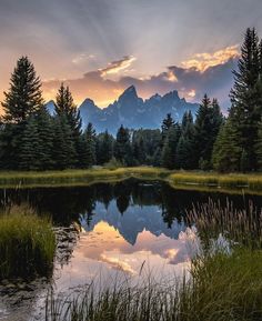 the sun is setting over a mountain lake with trees in the foreground and mountains in the background