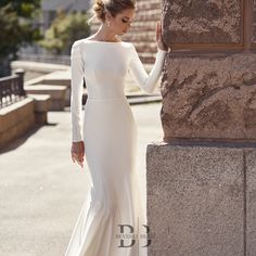 a woman in a long white dress leaning against a stone wall with her hand on the side