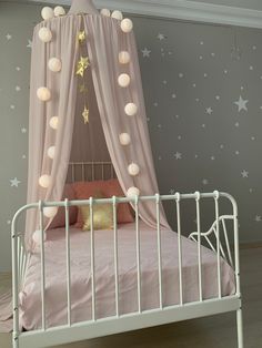 a white metal bed with pink sheets and stars on the wall behind it, in a girls'bedroom