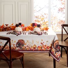 the table is set for thanksgiving dinner with turkeys and pumpkins on it, along with two chairs