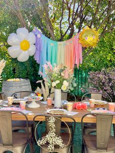 an outdoor table set up for a party with balloons and flowers in the background,