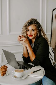 a woman sitting at a white table with a laptop and coffee in front of her